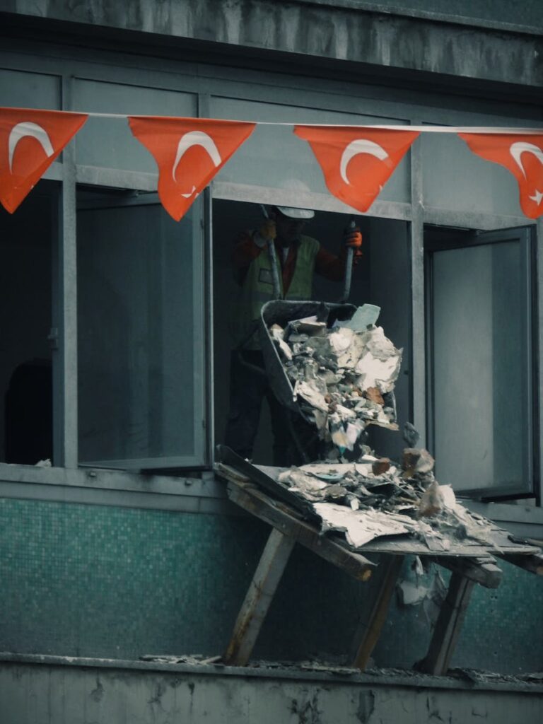 Worker throwing construction debris from a building window decorated with Turkish flags.