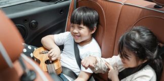 From above smiling ethnic boy and girl in casual outfits sitting fastened in passenger seats with ukulele during road trip together