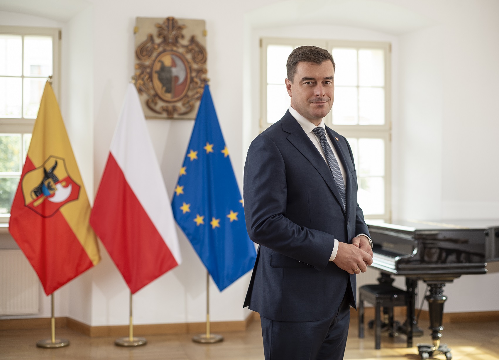 Meższyzna stojący przed flagami polską, unijną i miasta Leszno