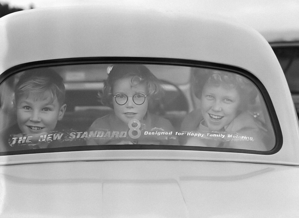 a black and white photo of three children in a car
