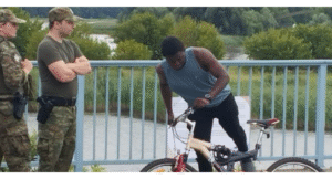 umundurowani ludzie zatrzymują na moście osobę na rowerze