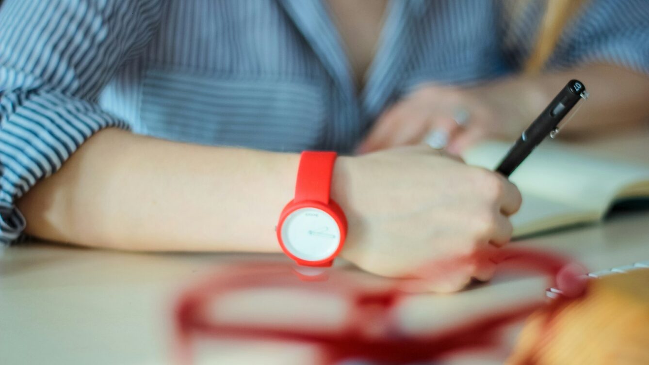 kobieta z czerwonym zegarkiem na nadgarstku i długopisem w ręku, by Eugene Chystiakov/unsplash
