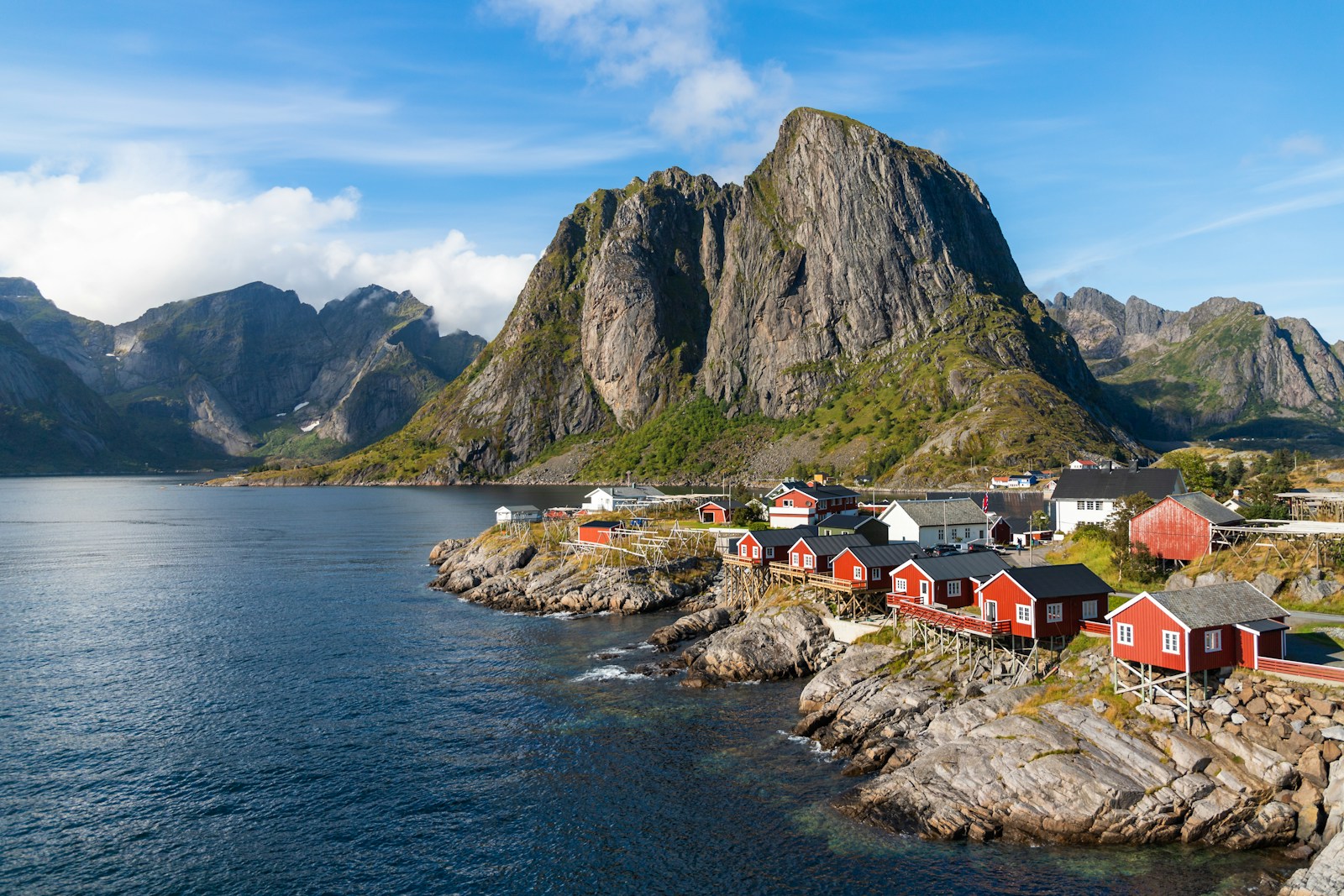 a group of houses by a body of water with mountains in the background with Lofoten in the background/ Photo by Benoît Deschasaux/Unsplash