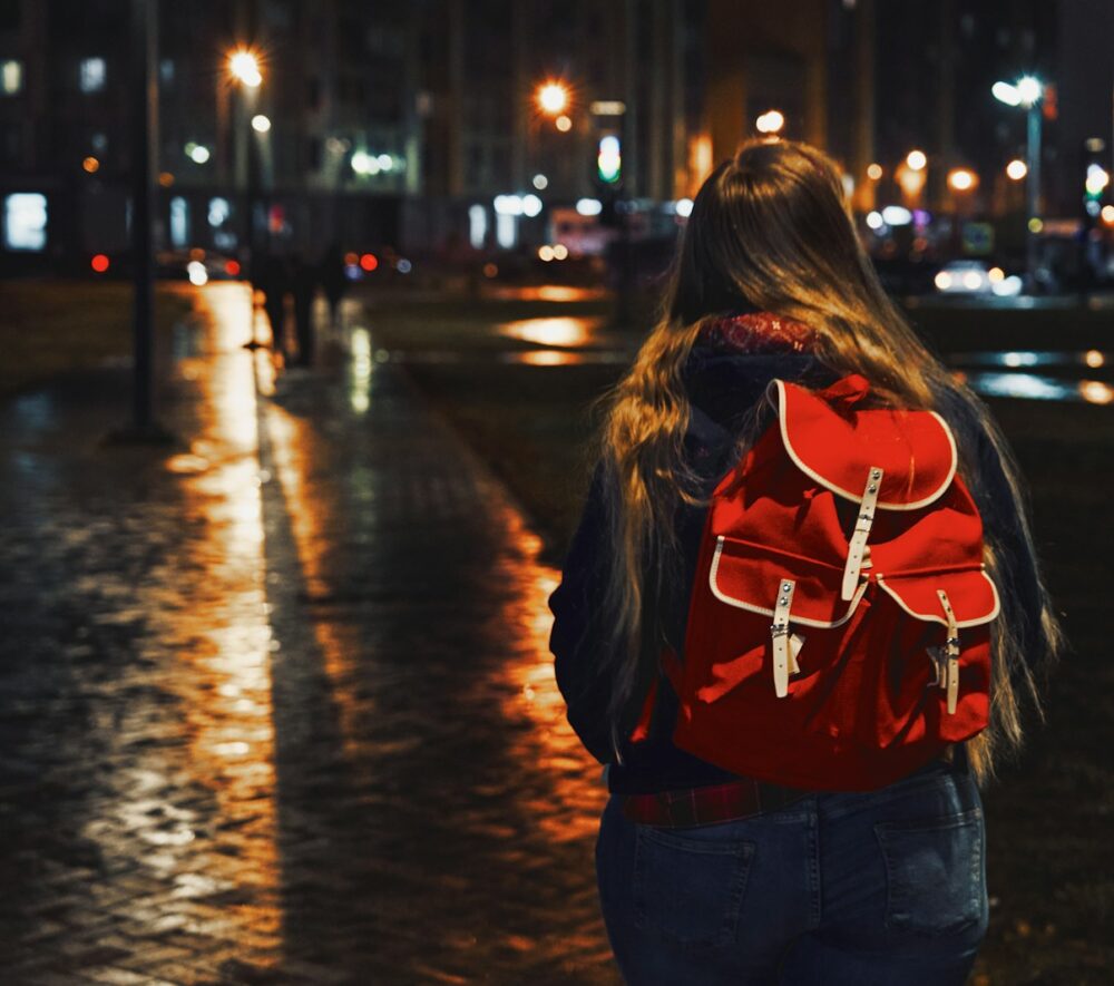 woman in red jacket and blue denim jeans walking on street during night time/ Maxim Tolchinskiy/ Unsplash