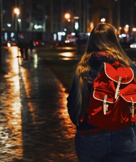 woman in red jacket and blue denim jeans walking on street during night time/ Maxim Tolchinskiy/ Unsplash