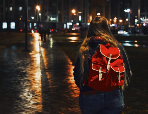 woman in red jacket and blue denim jeans walking on street during night time/ Maxim Tolchinskiy/ Unsplash