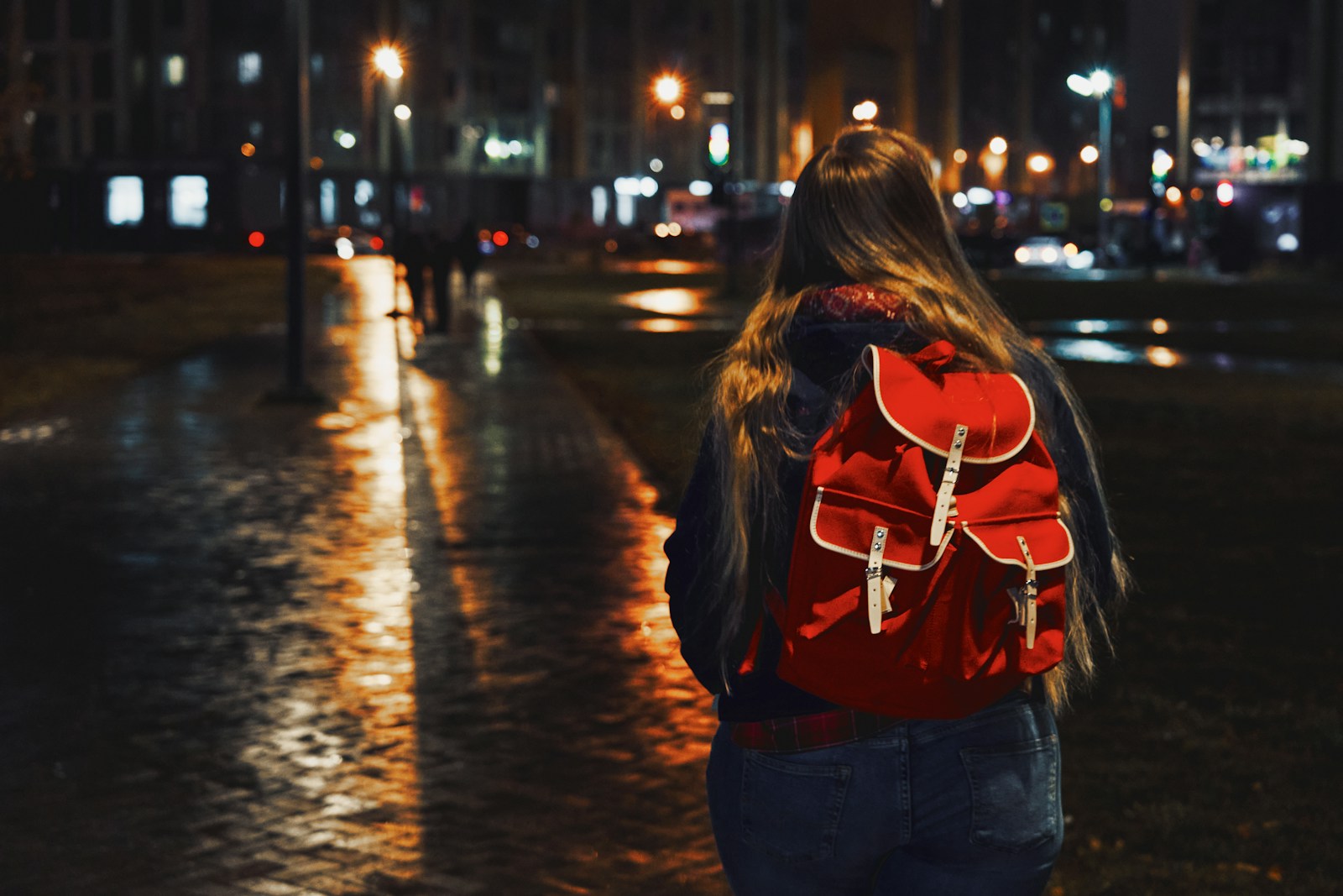 woman in red jacket and blue denim jeans walking on street during night time/ Maxim Tolchinskiy/ Unsplash