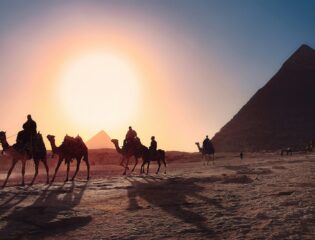 five persons riding camels walking on sand beside Pyramid of Egypt