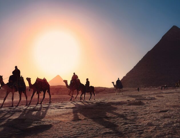 five persons riding camels walking on sand beside Pyramid of Egypt