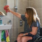 Woman in wheelchair cleaning bathroom mirror