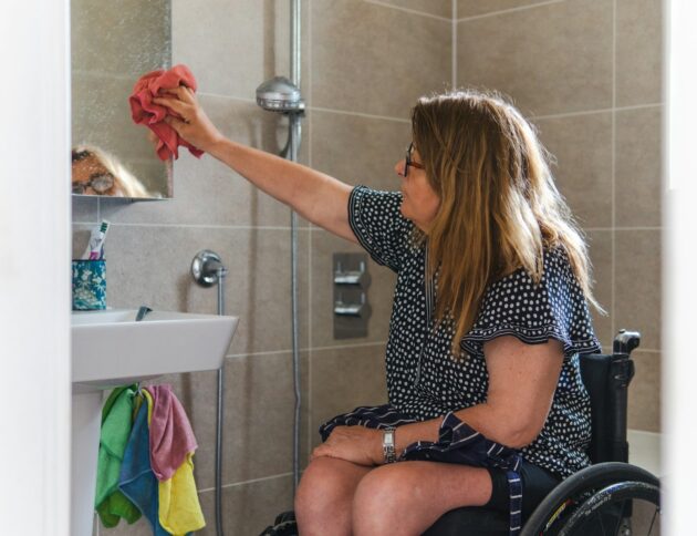 Woman in wheelchair cleaning bathroom mirror
