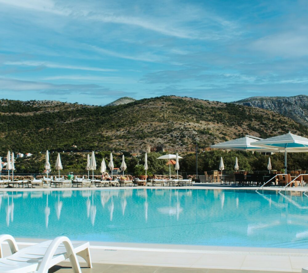 Resort swimming pool with lounge chairs and mountains.