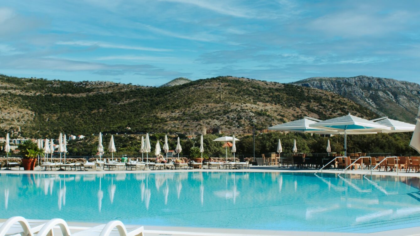 Resort swimming pool with lounge chairs and mountains.