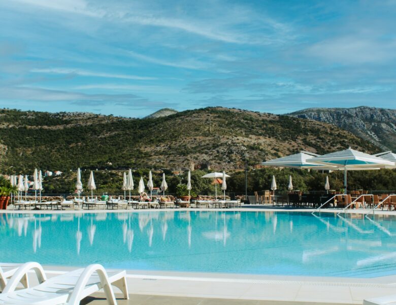 Resort swimming pool with lounge chairs and mountains.
