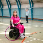 Woman in wheelchair with hula hoop, man in background